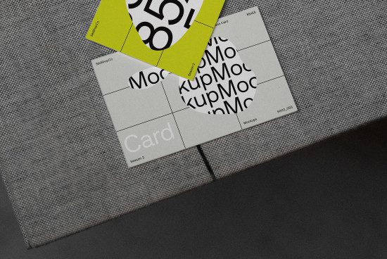 Business card mockup with modern design elements scattered on a textured grey fabric surface, providing a realistic presentation for branding.