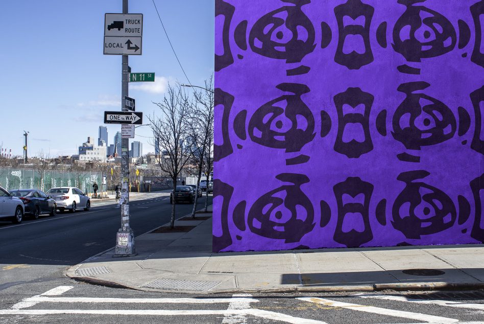 Urban street view with a vibrant purple graffiti wall, ideal for mockup background, featuring street signs, cityscape, and clear sky.