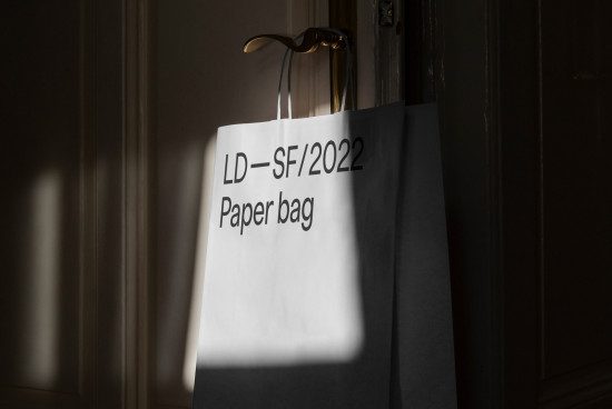 Elegant paper bag mockup hanging on a door handle in natural lighting, ideal for presenting branding projects to designers.