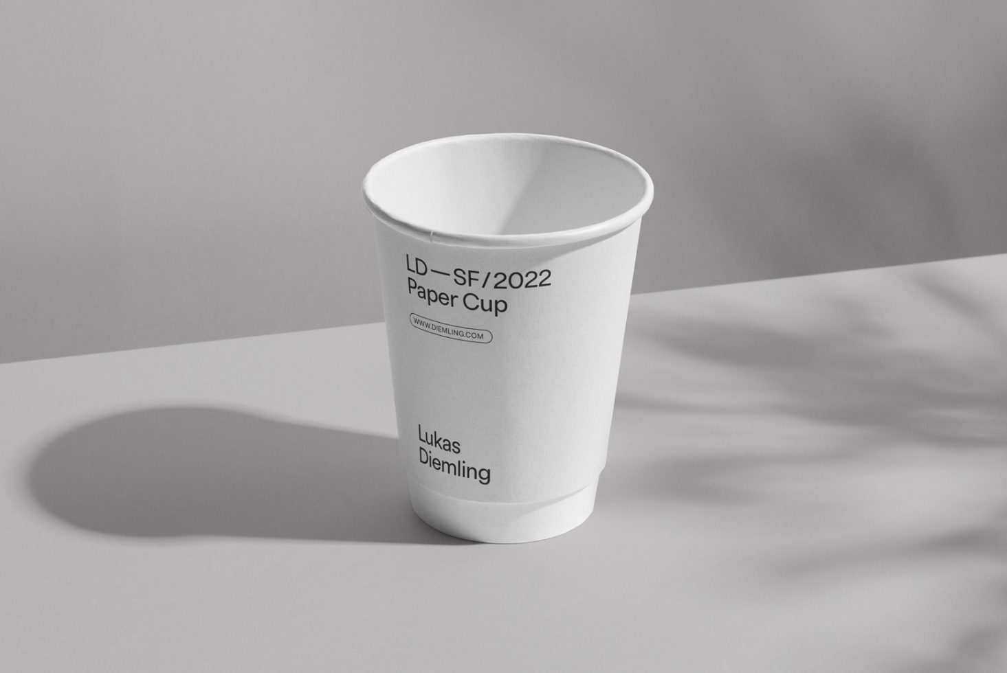 Minimalist paper cup mockup in black and white with subtle shadows, perfect for showcasing logo and branding designs.