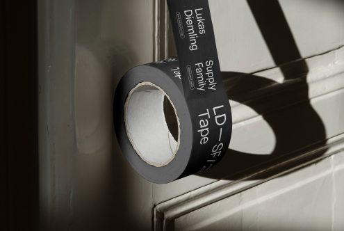 Roll of black duct tape with typography mockup casting shadow on white wall, useful for graphic design presentations.