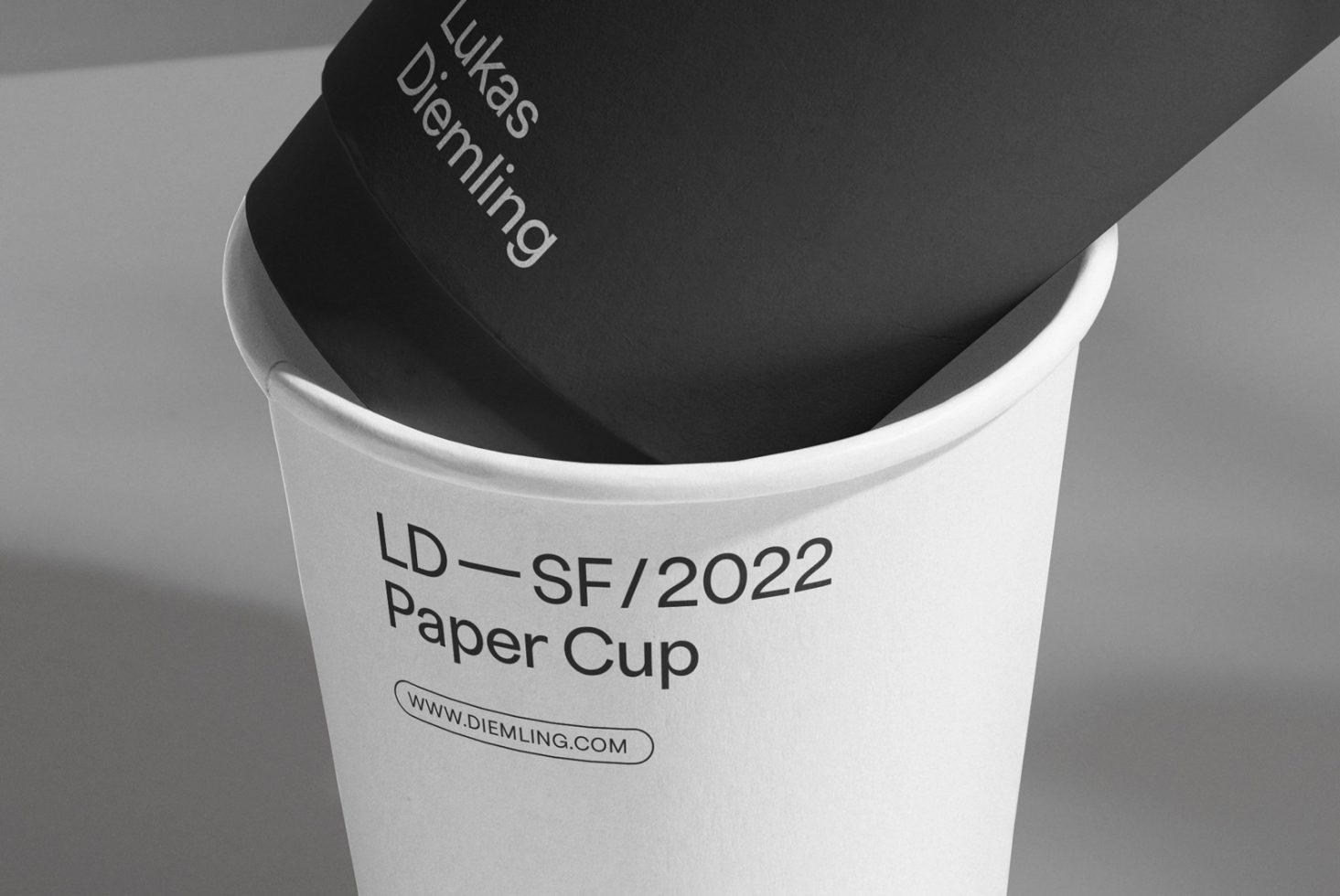 Close-up view of a black and white paper cup mockup with modern typography design, ideal for brand presentation and packaging design.