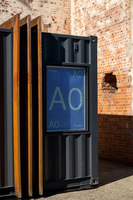 Urban poster mockup on outdoor container by brick wall, showcasing design space for advertising graphics in a realistic setting.