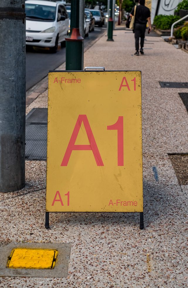 Yellow A-frame signboard on a sidewalk displaying text 'A1', suitable for mockup designs, displaying fonts or advertising templates.