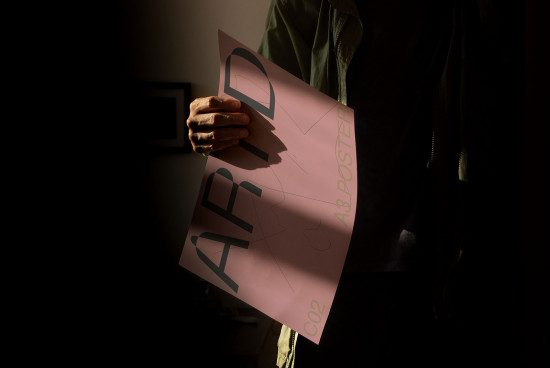 Person holding a graphic design poster mockup in a dimly lit room for designers and creative assets.
