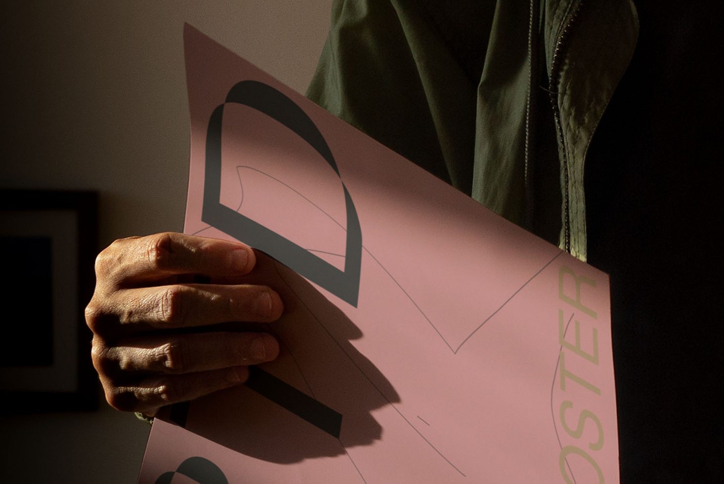 Person holding a poster mockup with a minimalist design in a dark room, ideal for showcasing graphic designs and prints.