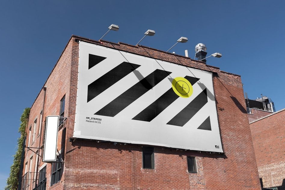 Building exterior billboard lit by daylight, black striped pattern, bright yellow dot accent, clear sky