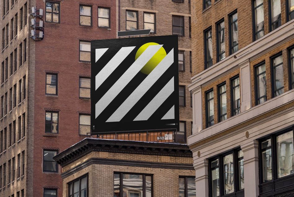 Building-mounted billboard between brick facades with black diagonal stripes, yellow sphere accent