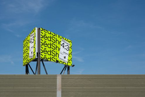 Billboard mockup with bright yellow background and bold black text, perched above a grey building against a clear blue sky, ideal for designers.