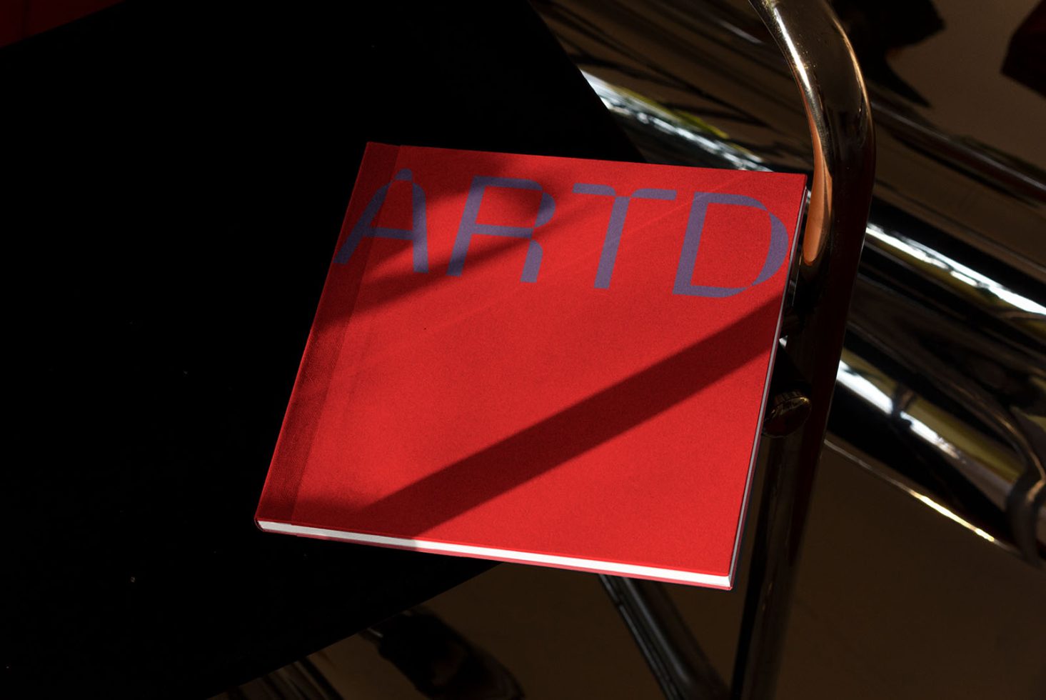 Red book cover mockup with ARTD text shadow on table, design presentation, graphic print showcase, modern style.