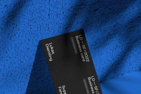 Elegant black business card mockup with clean design lying on a textured blue surface, perfect for professional branding and identity presentations for designers.