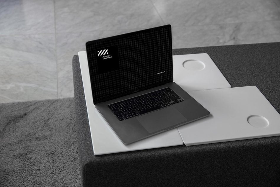 Laptop on desk with notebooks showing dark grid pattern screen, minimalist workspace setup
