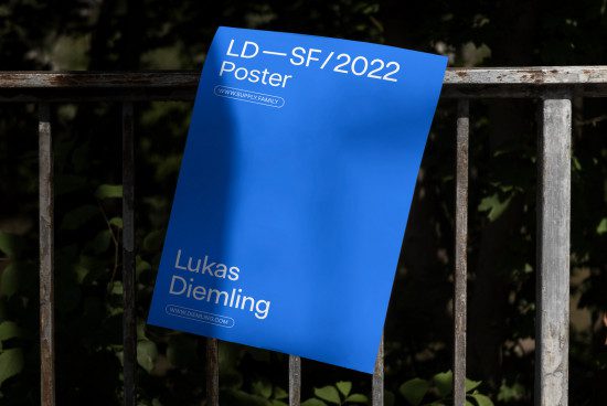 Blue poster mockup leaning on metal fence outdoors with clear text and website address, ideal for graphic designers, poster template.