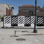 Urban streetscape with striped construction barrier graphic design, clear sky, and city buildings in background, ideal for mockup or urban template.