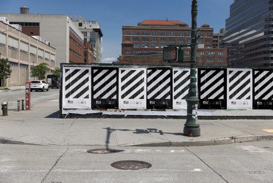 Urban streetscape with striped construction barrier graphic design, clear sky, and city buildings in background, ideal for mockup or urban template.