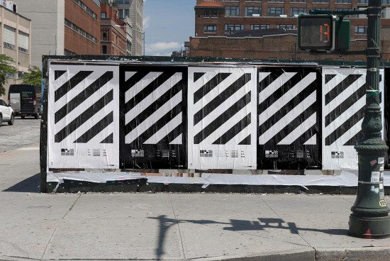 Urban construction mockup with black and white diagonal stripes and font samples on a temporary wall, daytime city setting. Graphic designers asset.