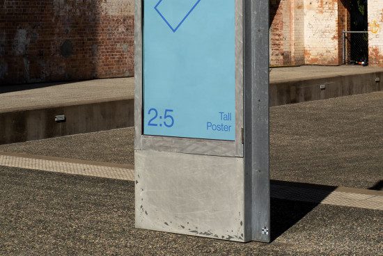 Urban outdoor advertising mockup featuring a tall poster on a metal information kiosk, brick wall background, and textured pavement.