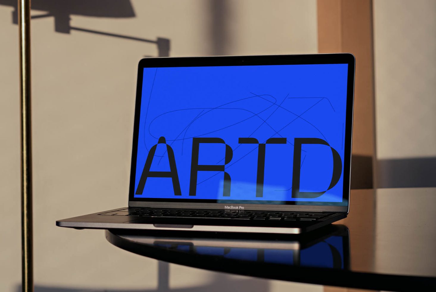 Sleek laptop showcasing bold font design in blue, ideal for graphics and templates, placed on a glass table with soft shadows.