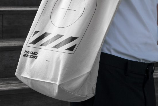 White tote bag mockup on a person's shoulder with bold black graphic design, ideal for showcasing branding designs to clients.