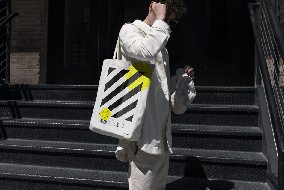 Person holding a tote bag with modern graphic design on urban steps, ideal for mockups, urban style, fashion accessory, designer bag template.