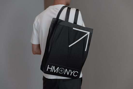 Man holding black tote bag mockup with graphic design, rear view, ideal for presenting branding projects to clients.