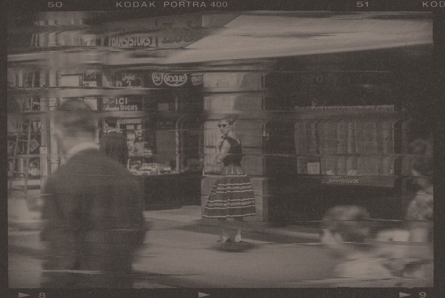 Vintage street scene with blurry figures, old storefronts, and a woman crossing, sepia-toned for retro graphics or mockup backgrounds.