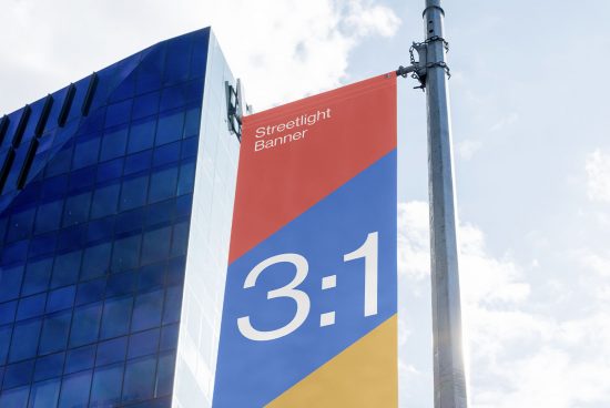 Streetlight banner mockup on a pole with a modern building background, featuring a clear sky for design presentation.