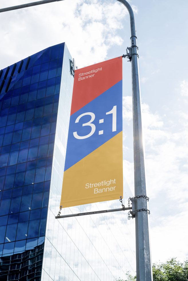 Outdoor streetlight banner mockup hanging on lamp post with city building background, clear sky, design presentation template.