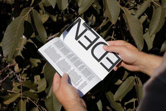 Person holding open magazine mockup with bold typography in natural setting, showcasing clear print design layout for graphic designers.