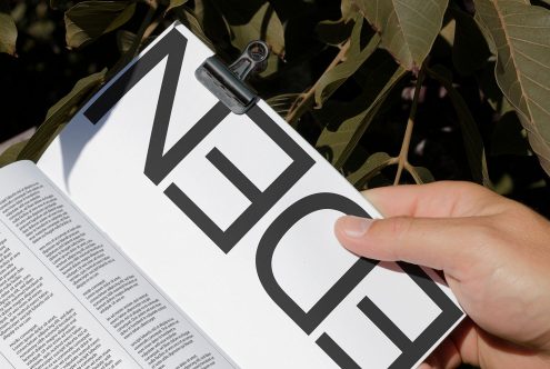 Hand flipping through a book with bold typography, showcasing modern font design for graphic and print projects, natural light, and foliage background.