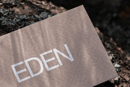 Elegant paper mockup with reflective silver text EDEN on a textured rock showcasing modern font design and presentation for branding.