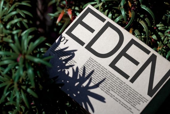 Magazine mockup with large bold typography on cover, resting in natural green shrubbery, showcasing contrast and layout design.
