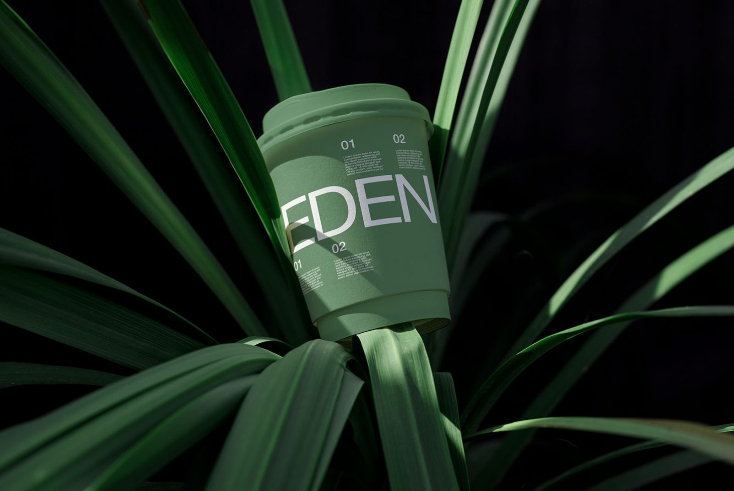 Green coffee cup with modern typography mockup nestled in leaves, ideal for eco-friendly branding presentation.