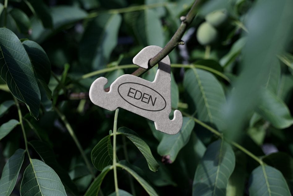 Metal garden tag with EDEN branding attached to thin plant branch outdoors