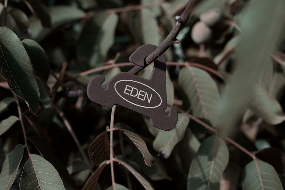 Dark metal plant marker with EDEN logo clipped to branch with reddish stems