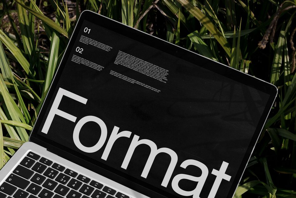 Laptop screen with bold format typography surrounded by green foliage, perfect for mockup, graphic design, web template, digital asset.