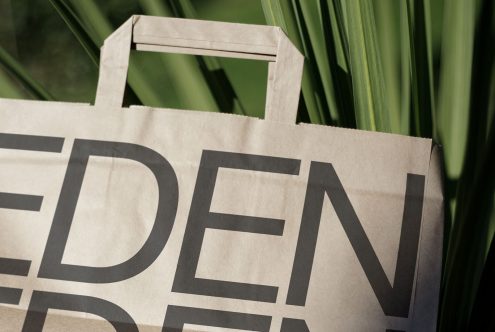 Paper bag with bold typography design displaying the word EDEN, set against a natural green plants background, ideal for eco-friendly mockup.