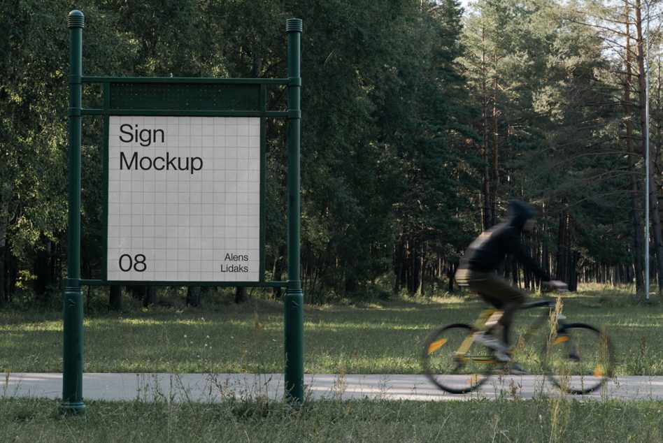 Outdoor sign mockup with white panel on green metal frame, cyclist riding past