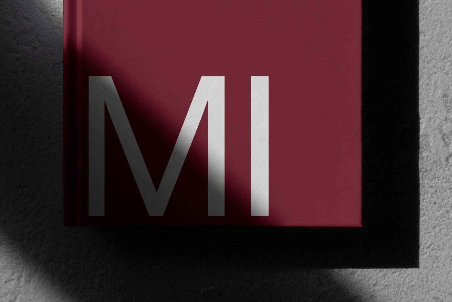 Creative mockup of red book cover with bold white letter M design casting shadow, ideal for graphic design and branding presentations.