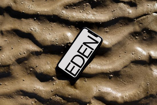 Smartphone on wet sand displaying word EDEN for mockup, showcasing modern font design and natural textures for creative projects.
