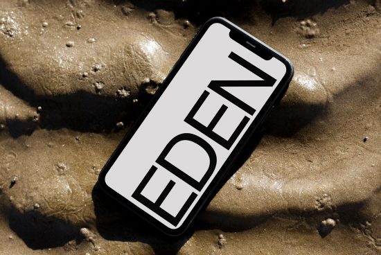 Smartphone mockup on sandy beach surface, displaying bold 'EDEN' text, ideal for showcasing design work and app interfaces for designers.