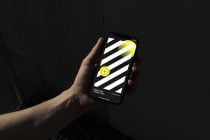 Hand holding dark striped phone mockup with bright yellow circular element
