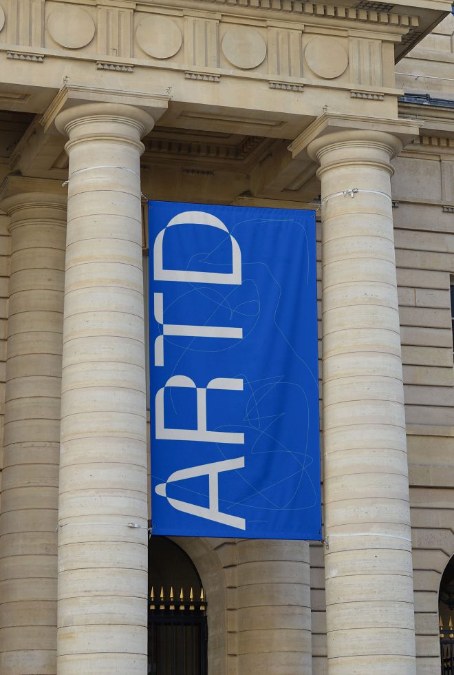 Vertical blue banner with bold white text mockup hanging between stone pillars, ideal for designers to showcase branding and advertising designs.