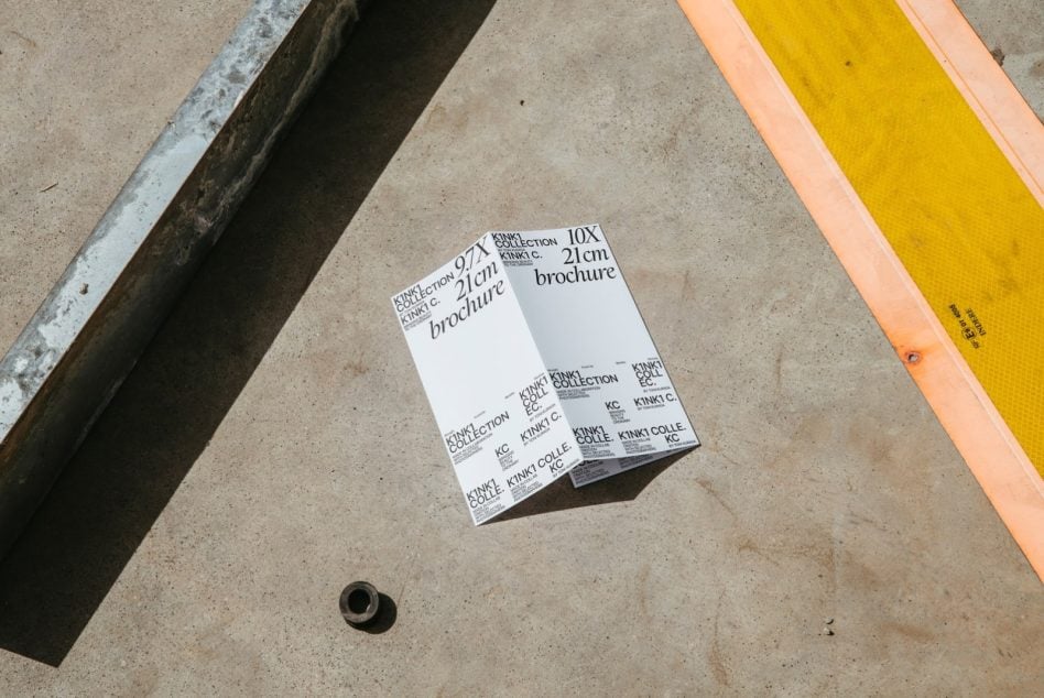 Folded brochure mockup displaying KINKI collection typography on industrial concrete