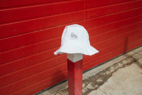 White bucket hat with logo mockup on pole against red background, urban fashion accessory template for design presentation.