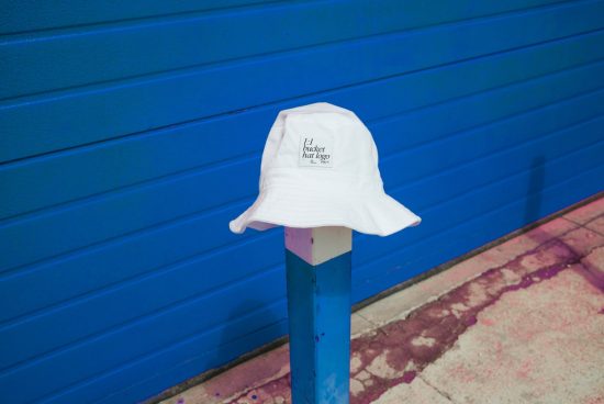 White bucket hat with logo mockup placed on outdoor blue post for fashion and accessory design presentation.