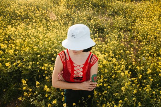 Woman in red top and white bucket hat standing in yellow flower field, summer fashion mockup with space for logo design.