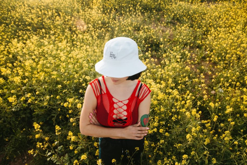 White bucket hat on person in red mesh top surrounded by yellow wildflowers