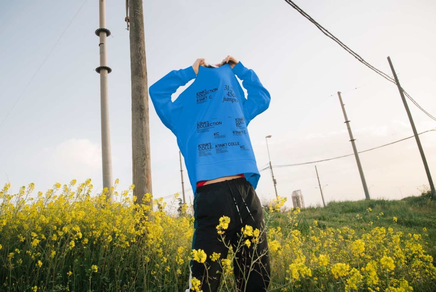 Person in blue sweatshirt forming heart shape with hands in blooming field, for fashion mockup, outdoor apparel design template.