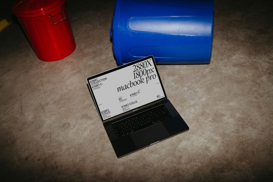 Laptop mockup on floor showing screen resolution details for design presentation, near red and blue containers, digital asset for designers.